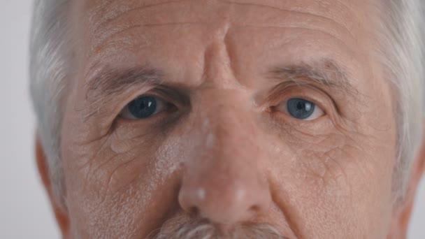 Zbliżenie na starszy człowiek z wąsem wygląda do aparatu na białym tle - Materiał filmowy, wideo