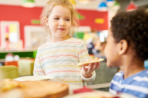 Kolorowy portret dzieci jedzenie pizzy, ciesząc się niesamowitą zabawę w kawiarni, koncentrują się na słodkie blond dziewczyna oferuje pizza do przyjaciela - Zdjęcie, obraz