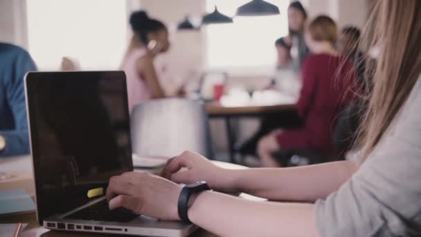 Gros plan de jeunes mains féminines méconnaissables avec bracelet intelligent tapant sur un ordinateur portable près de la table, travail d'équipe en arrière-plan
. - Séquence, vidéo