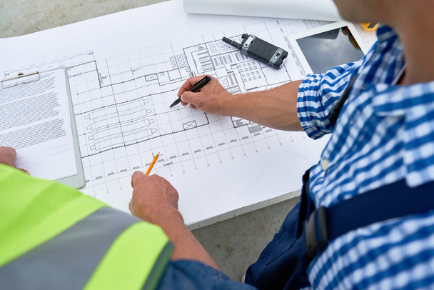 Plan rapproché à angle élevé de deux travailleurs de la construction qui examinent les plans d'étage et la documentation technique sur place
 - Photo, image