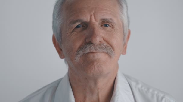 Portret van Senior man met snor kijkt naar camera op witte achtergrond - Video