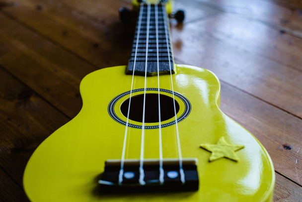 Petit ukulélé jaune sur sol en bois prêt à être joué
 - Photo, image
