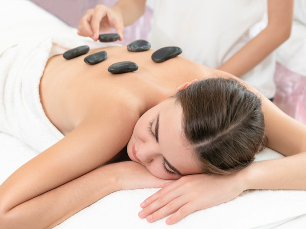 Kobieta dostaje gorące kamienie masażu leczenie przez profesjonalnego kosmetyczka w salonie spa. Luksusowe wellness, odciążenie pleców i koncepcja odmłodzenia. - Zdjęcie, obraz
