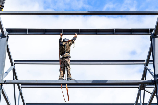 建設保険なし制服で男ビルダーは地上高 mettalical 構造物の建設に移動します。建設現場での安全に対する侵犯 - 写真・画像