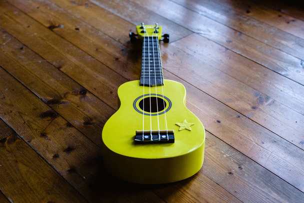 Petit ukulélé jaune sur sol en bois prêt à être joué
 - Photo, image