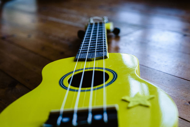 Pieni keltainen ukulele puulattia valmis soitettavaksi
 - Valokuva, kuva