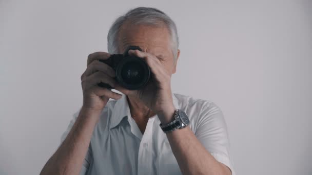 灰色髪シニア男カメラマンはカメラでショット彼写真ホワイト バック グラウンドで - 映像、動画