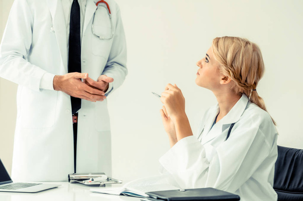 Young female doctor at hospital office having conversation talking with another male doctor standing beside the table. Concept of medical healthcare professional team. - Foto, Imagem