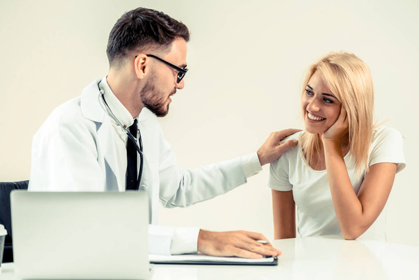 Male doctor talks to female patient in hospital office while writing on the patients health record on the table. Healthcare and medical service. - Photo, Image