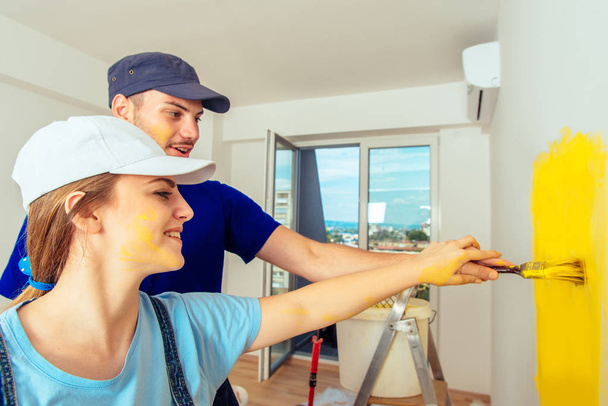 Girl painting wall with yellow paint while her boyfriend holding her hand - Foto, Imagen