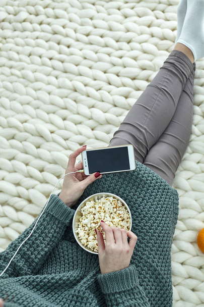 Nagyon hangulatos kép az ősszel, szeptember, október, November. Egy lány néz filmet, a telefon-val fejhallgató, és pattogatott kukoricát eszik. Zöld képernyő a mobil a kép, szöveg, információ. - Fotó, kép