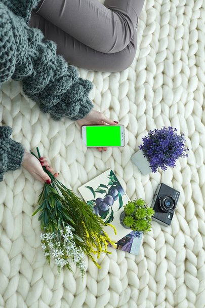 秋、9 月、10 月、11 月の非常に居心地の良い画像です。温かみのあるグリーンのセーターの女の子は柔らかいニット格子縞のある、彼女の手で野生の花の花束を保持します。携帯電話と本. - 写真・画像