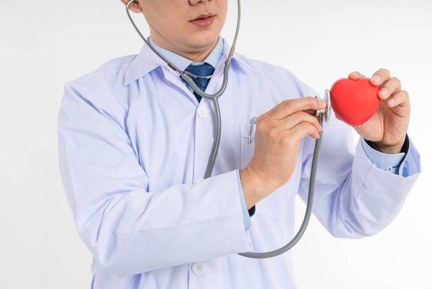 Beyaz üniformalı erkek doktor tutun ve stetoskop kalp kırmızı oyuncak kalbini kontrol etmek için kullanın. Kardiyo therapeutist, hekim yapmak kalp kalp hızı ölçü birimi, aritmi concep fiziksel, - Fotoğraf, Görsel