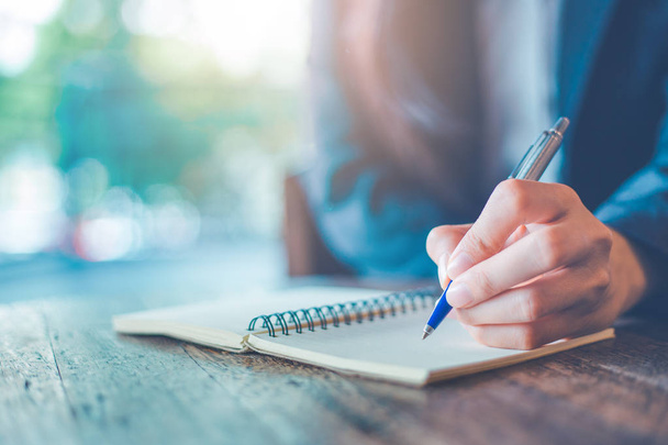 Femme d'affaires écriture à la main sur un bloc-notes avec un stylo dans le bureau
. - Photo, image