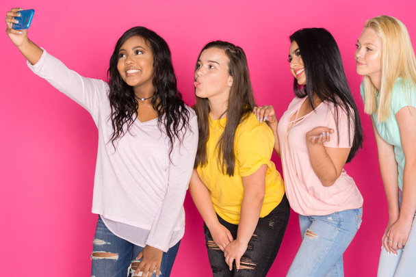 Grupo de quatro meninas adolescentes se divertindo juntos em um fundo rosa
 - Foto, Imagem