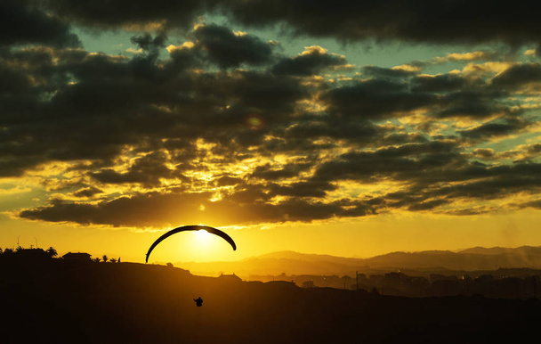 a beautiful background with a silhoutte of a paraglider, in front a of a setting sun. - Valokuva, kuva