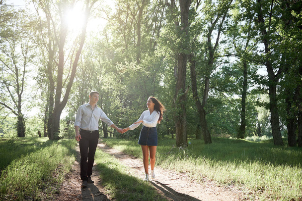 young couple walking in the forest, summer nature, bright sunlight, shadows and green leaves, romantic feelings - Photo, Image
