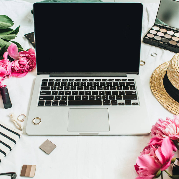 Lapos feküdt, top női irodai íróasztal munkaterület megtekintése ál fel a laptop, rózsaszín bazsarózsa virágok csokor, kiegészítők és kozmetikumok. Divat, szépség, vagy életmód blog koncepció. - Fotó, kép
