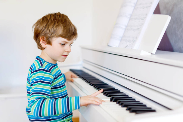 Bonito menino saudável tocando piano na sala de estar ou escola de música. Criança pré-escolar se divertindo com a aprendizagem de tocar instrumento de música. Educação, conceito de competências
 - Foto, Imagem