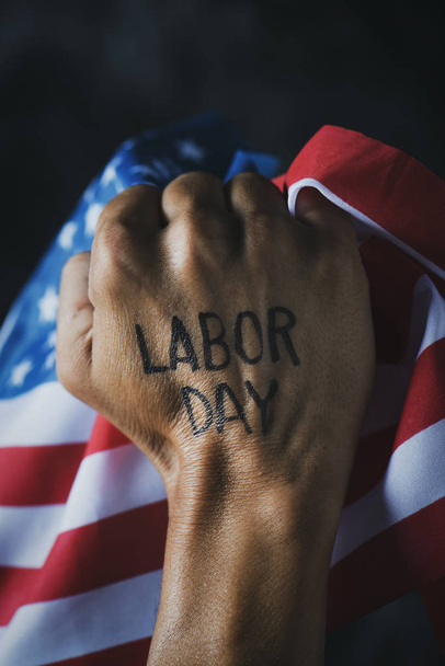 closeup of the raised fist of a young man with the text labor day handwritten in it, and the flag of the United States - Photo, Image