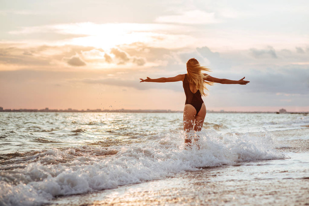 Ulkona elämäntapa muotokuva kaunis tyttö musta uimapuku. Nuori hipsterinainen leikkii hiuksillaan. Hän on onnellinen. Aurinkoinen kuuma kesäpäivä trooppisella valtameren rannalla
. - Valokuva, kuva