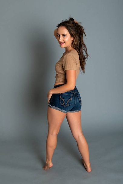 Beautiful petite brunette in a tan knit top and denim shorts - Fotografie, Obrázek