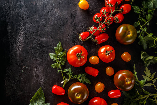Fresh tomatoes on a black background with leaves. Top view with copy space - Foto, Bild