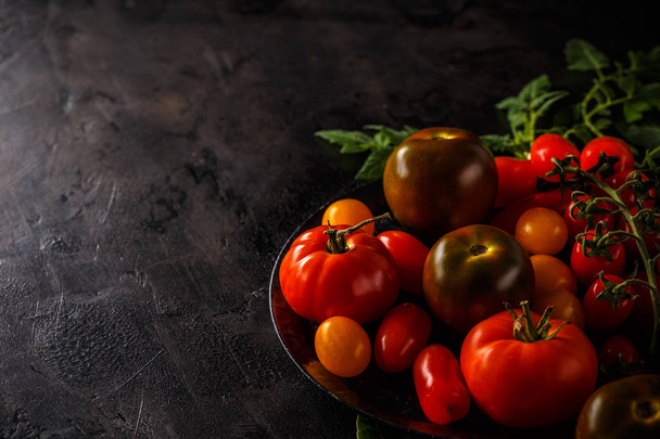 Fresh tomatoes on a black background with leaves, space for your text - Fotografie, Obrázek