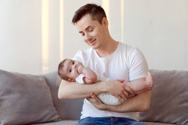 Kanepede oturan ve bebek ellerinde tutan genç baba - Fotoğraf, Görsel