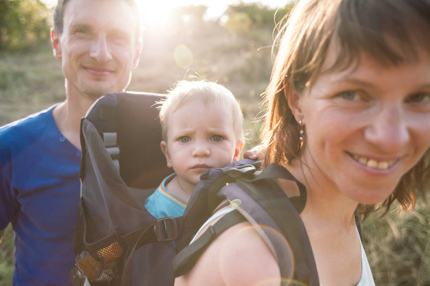 Семья путешествует с ребёнком. Женщина носит своего сына в рюкзаке. Муж и жена увезли ребёнка в горы. Путешествует с детьми. Мужчина идет со своей семьей
. - Фото, изображение