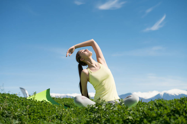 slender flexible girl meditating in a park on green grass in the sun, doing yoga - Foto, Imagem