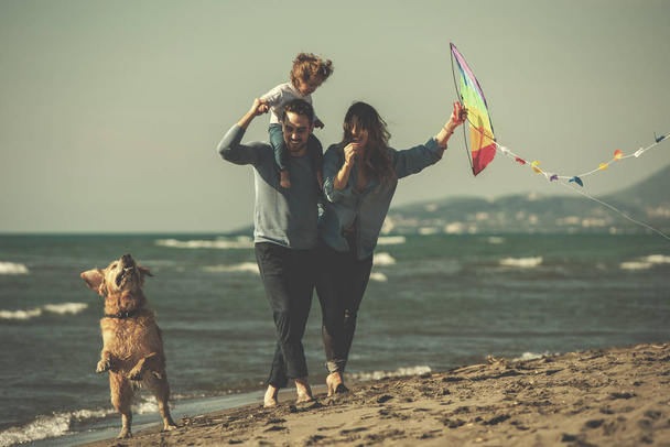 秋の日のフィルターの間にビーチで犬と凧で楽しんでいる子供たちと幸せな若い家族 - 写真・画像