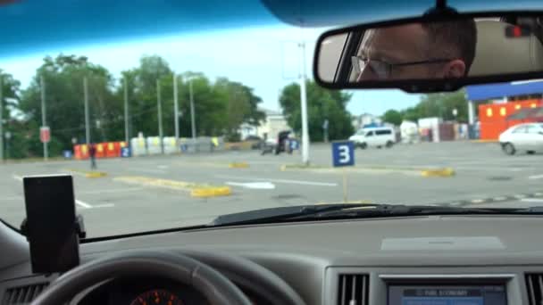 Persoon veel rondrijden te vinden parkeren spaceperson bril gedeeltelijk zichtbaar in de spiegel rijden auto rond veel te zoeken naar parkeerplaats naast grote rode vrachtwagen. - Video