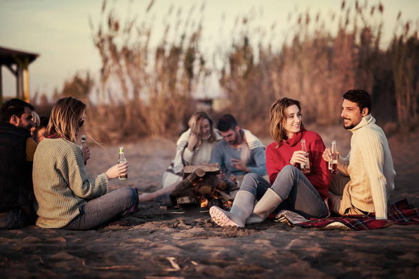 Young Couple enjoying with friends Around Campfire on The Beach At sunset drinking beer filter - 写真・画像