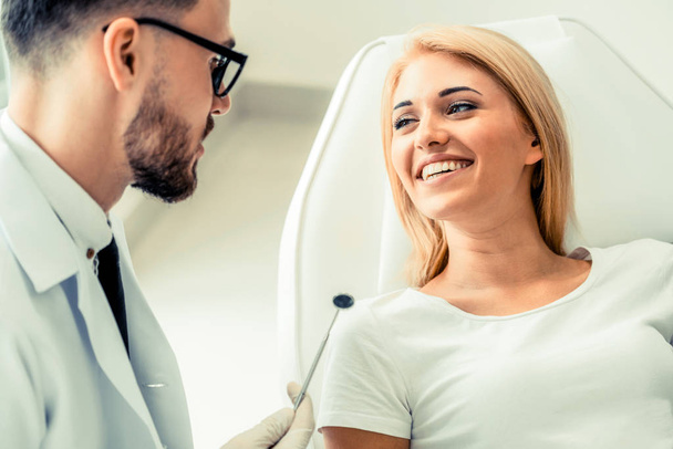 Mladý pohledný zubař rozhovory s šťastná žena pacient sedí na židli zubního lékaře v zubní klinice. Koncepce péče stomatologie. - Fotografie, Obrázek