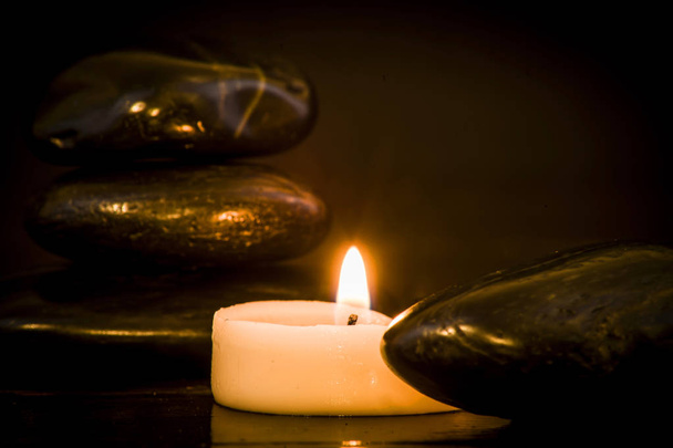 Dark stones and lit candle on a dark background - Foto, afbeelding