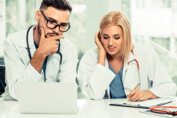 Young female doctor works at office in hospital while talking to male doctor sitting beside her. Medical service and healthcare concept. - Zdjęcie, obraz