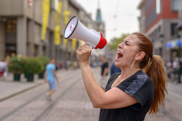 Женщина, кричащая в мегафон на городской улице, выражая свою неприязнь во время протеста или демонстрации вблизи ее лица
 - Фото, изображение