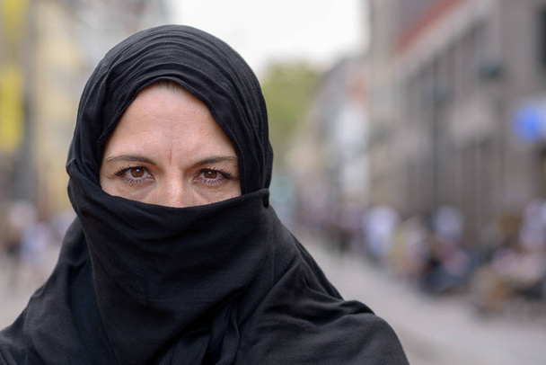Mulher muçulmana vestindo um hijab preto ou lenço de cabeça na cidade de pé ao ar livre na rua com espaço de cópia
 - Foto, Imagem