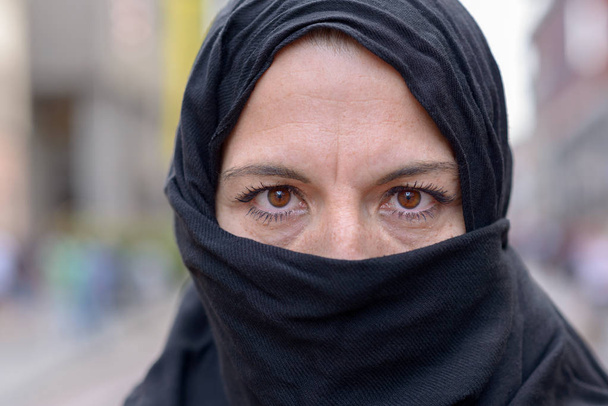 Muszlim nő visel egy fekete hidzsáb vagy fejkendő, a város kint állt az utcára nézett elgondolkodva a kamera - Fotó, kép