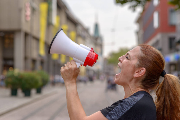 Žena křičí do tlampačem na městské ulici vyjadřovat její displaeasure během protestu nebo demonstrace zblízka boční pohled na její tvář - Fotografie, Obrázek