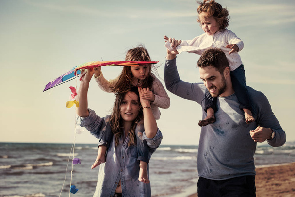 young family with kids resting and having fun with a kite at beach during autumn day filter - Foto, afbeelding