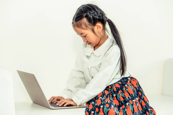 Маленька щаслива дитина, використовуючи ноутбук, сидить на білому дивані. Дитячий спосіб життя
. - Фото, зображення