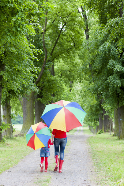 mother and her daughter with umbrellas in spring alley - Photo, Image