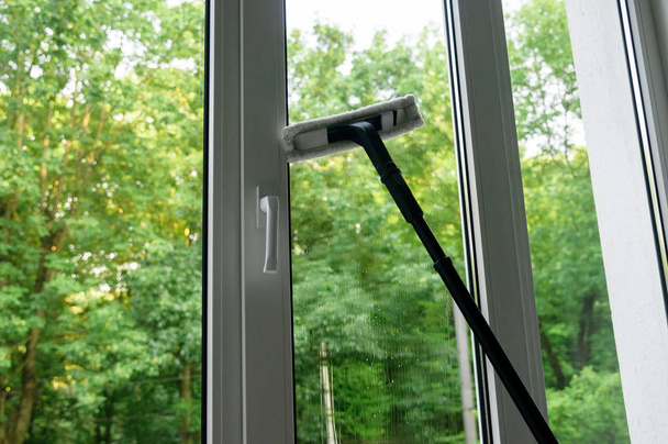 cleaning of plastic vinyl window with squeegee on green trees background - Photo, Image