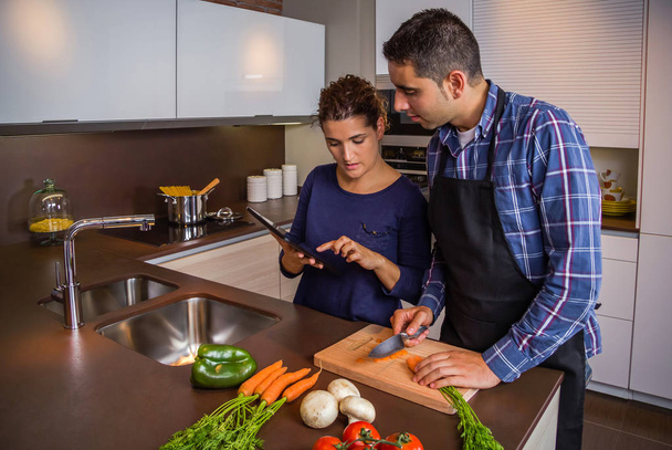 Couple in home kitchen looking recipe with a electronic tablet - Photo, Image