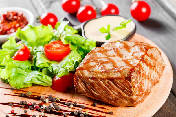 Grilled steak pork with fresh vegetable salad, tomatoes and sauce on wooden cutting board. - Photo, Image
