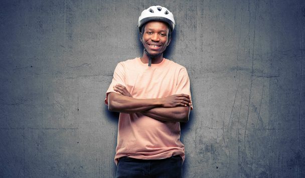 Чорний чоловік у велосипедному шоломі з перехрещеними руками впевнений і щасливий з великою природною посмішкою сміється
 - Фото, зображення