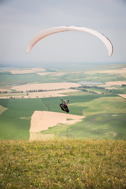 White orange paraglide with a paraglider in a cocoon against the background of fields of the sky and clouds. Paragliding Sports - Фото, изображение