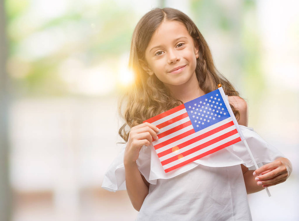 Brunette hispanic girl holding flag of United States of America with a happy face standing and smiling with a confident smile showing teeth - Fotó, kép